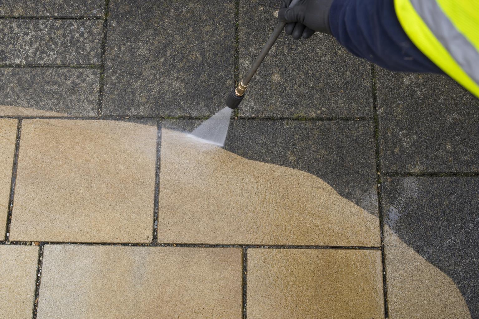 Close-up of a power-washed paving slab showing a clean strip next to the dirty, algae-stained surface